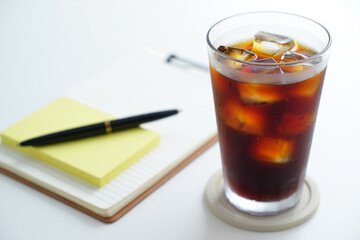 Iced Coffee with Notebook and Pen on White Table Refreshing Drink for Work or Study Beverage in Glass Cold Brew with Ice Cubes