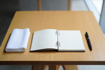 Open Notebook with Grid Paper Ready for Writing Next to White Towel and Pen on Wooden Tabletop Creates Inviting Workspace