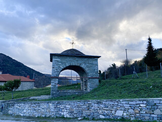 Obraz premium Rustic stone archway with cross set against serene mountain landscape at dusk