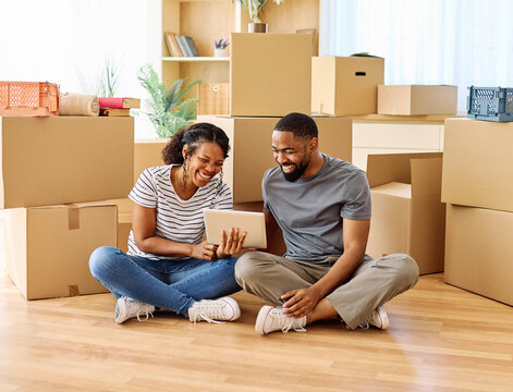 Portrait of a young couple unpacking, moving in and relocation to a new apartment, happy young couple  using a tablet, browsing and shopping online, , family new beginning sitting on the floor - Powered by Adobe