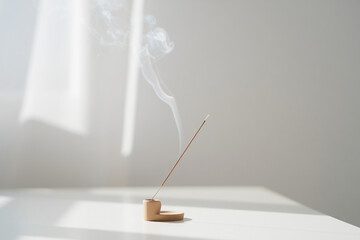 Incense stick burning creating smoke with home fragrance for calm and cozy minimalist living space aromatherapy on white table in the room