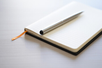 Notebook with Silver Pen and Orange Bookmark on Light Desk Top in Bright Room Interior at Home or Office Space in Minimalist Style 150chr