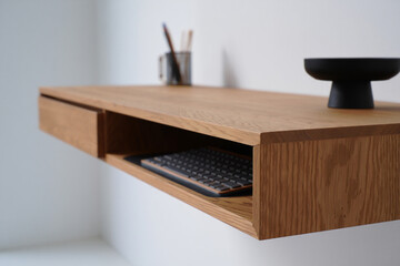 Floating Wooden Desk Mounted on a White Wall, Showing a Keyboard in the Cubby, with Desk Organizer and Bowl in a Modern Office Space 150chr