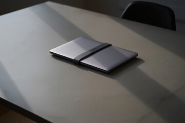 Closed Laptop with Elastic Strap on Top of Gray Table Surface in Natural Sunlight Creating Modern and Minimalist Aesthetic Workplace Scene