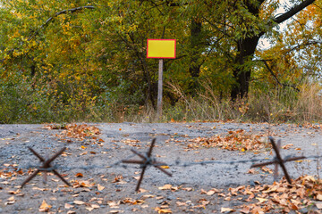 Barbed wire and blank sign at a rural crossroads during autumn sunrise in a quiet wooded area