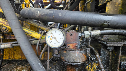 Close-up of a weathered industrial pressure gauge with rust and moisture, showing mechanical details and engineering atmosphere