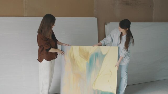 Two women collaborate in an art studio, showcasing their vibrant painting and creative process in a bright workspace