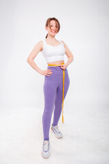 Beautiful sports girl measuring her waist with a measure tape isolated on a white background. Attractive young woman in sportswear posing in the studio.