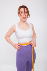 Beautiful sports girl measuring her waist with a measure tape isolated on a white background. Attractive young woman in sportswear posing in the studio.