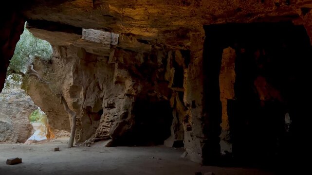 Expansive chamber inside Fabrika Hill Cave Complex where two people walk across the dim cavern floor, framed by rugged stone walls, natural openings and warm reflected light