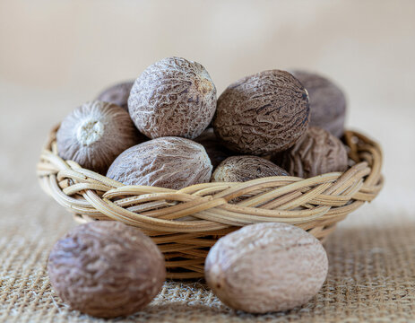 Whole jaifal nutmeg (Myristica fragrans) in a woven basket on jute surface, showing natural textured shells in warm soft light. Ideal for spice, herb, food and Ayurveda concepts.