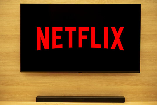 Netflix logo on a smart TV. The backdrop is a modern, minimalist oak wall. A simple soundbar completes the look.