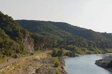 Picturesque landscape with a winding river, tree-covered hills, and a trail with people enjoying the outdoors on a beautiful day.