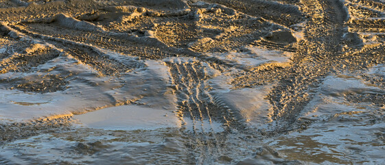 Traces de pneus de voiture dans la boue fraîche, mises en relief dans une lumière froide un soir d'hiver, format bannière