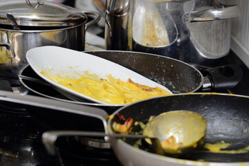 Pile of dirty pots and pans with leftover pasta on a messy stovetop