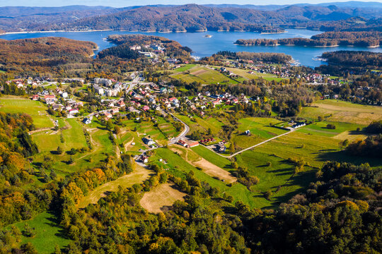 Wide aerial panorama of Polańczyk village and the Solina Lake (Jezioro Solińskie) in Bieszczady, Poland. Scenic October landscape with dam structure in the background.