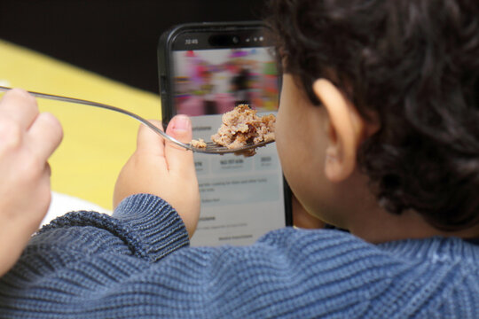 Child watching smartphone cartoon while being fed food with a fork