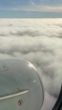 Vertical video. View from an airplane window flying slightly above a dense layer of cumulus clouds.