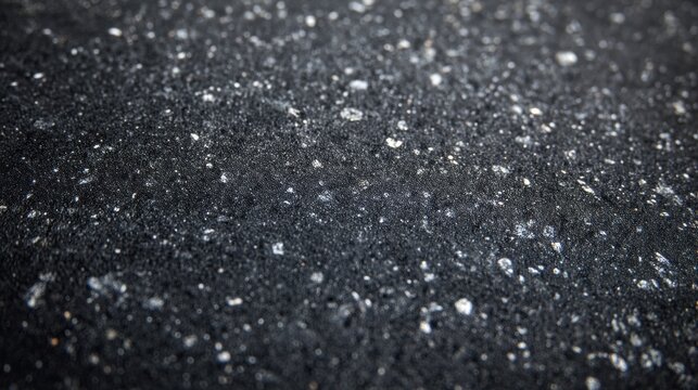 A close-up view of a black textured surface with scattered light reflections. It showcases the subtle details of the material's texture and sheen.