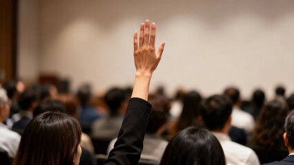 Close-up of a participant's hand raised, asking a question or voting during a professional conference or seminar, highlighting active engagement and communication.
