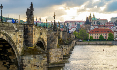 Colorful Prague skyline with the iconic Charles Bridge, baroque domes, and historic towers along the Vltava River. Stone arches, statues, and warm sunset light create a timeless European scene.