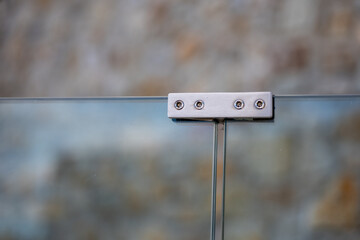 Close-up of a stainless steel connector joining two glass panels in a modern railing or fence.