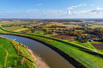 Wide aerial drone view of the Vistula River (Wisła) near Ispina village, Krakow area, Poland. Scenic landscape featuring flood embankments, rural houses, and a cycling route.