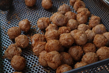 A close-up shot of numerous golden-brown, crispy, round fried taro balls draining in a metal fryer basket or colander.