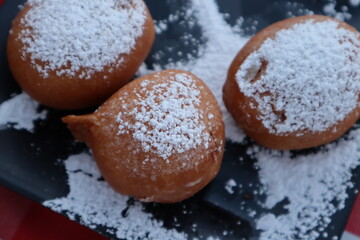 High-angle close-up of three traditional banana fritters generously dusted with powdered sugar, served on a black plate.