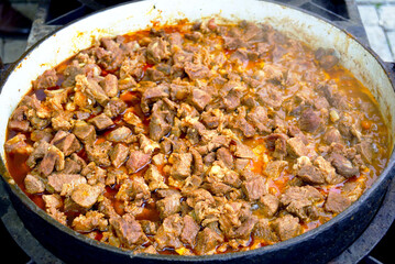 Diced meat chunks simmering in sauce inside a large cast iron pan. Represents goulash preparation, traditional stew making, hearty comfort food, slow cooking method, and Hungarian cuisine.