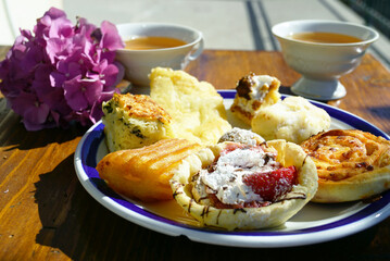 Assortment of sweet pastries, tea cups, and fresh pink hydrangea in sunlight. Symbolizes continental breakfast spread, homemade bakery selection, morning tea ritual, and leisurely brunch experience.