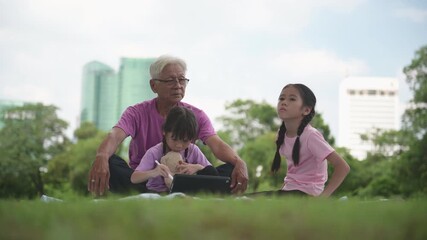 Happy Asian family children using tablet with her grandfather in the park	 - Powered by Adobe