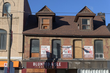 Fototapeta premium historic building facade with for sale signs and Blunted Aisle Cannabis ghost display at 668 Queen St E, Toronto