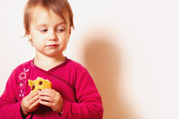 Child in a pink outfit eating a sweet treat with calm curiosity.