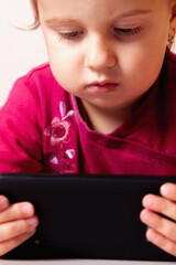 Little girl looking at the camera with a cheerful smile and a tablet. Vertical image.