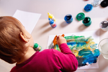 Little girl squeezing glue onto a colorful painting during an art activity.