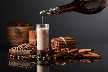 Coffee liquor is poured from a bottle into a glass with cream.