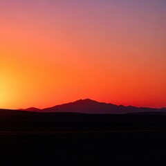 Peaceful golden hour over a vast landscape. The vibrant sunset paints the sky above the sharp, dark silhouette of hills at the serene horizon, open space, nature, scenic