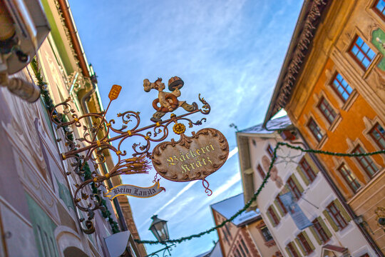 Partenkirchen, Bavaria, Germany &ndash; Nov 28, 2025: An ornate wrought-iron bakery sign reading "B&auml;ckerei Kr&auml;tz" hangs along Ludwigstra&szlig;e, framed by colorful frescoed buildings under the winter sky.