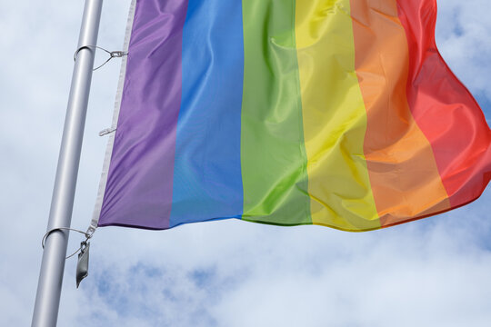 LGBT Pride flag waving in sunlight against blue sky - Powered by Adobe