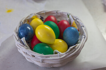 A small woven basket full of brightly colored Easter eggs in blue, yellow, green and red. The basket is placed on a light, slightly blurred background
