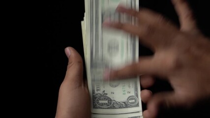 Hands are handling a stack of united states one dollar bills against a dark backdrop in a blurred motion possibly counting the cash