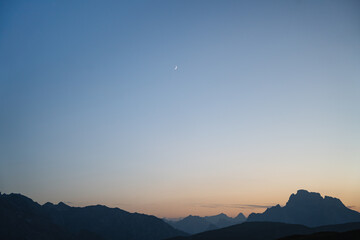 Minimalist mountain landscape at dusk with a crescent moon and soft pastel sky over the Dolomites. Calm, serene and atmospheric nature scenery.