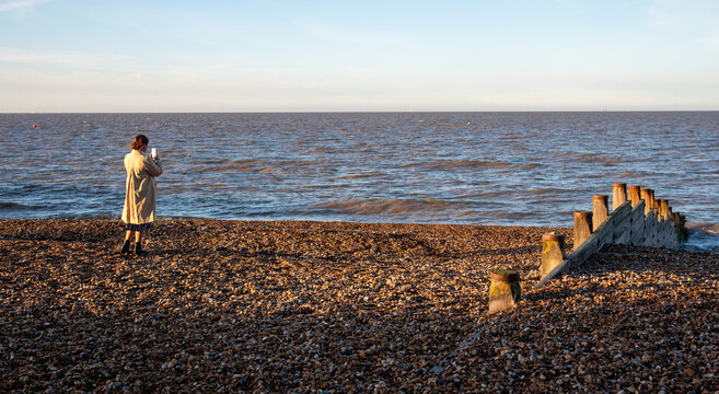 Woman photographing sea on pebble beach during sunset