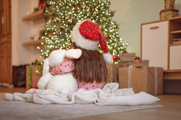 The kid sits near the Christmas tree in the house on the eve of the winter holidays. Happy childhood.