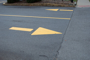 painted yellow directional arrows on asphalt road surface, traffic markings in parking lot or driveway.
