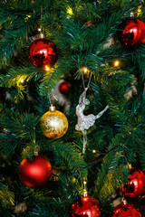 Red and gold balls and an elegant silver ballerina on a tree in the soft glow of garlands. Classic Christmas aesthetic and cozy atmosphere