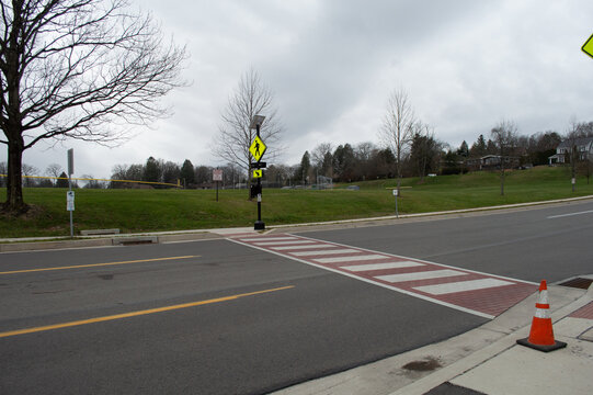 Residential street scene featuring a pedestrian crosswalk with red striped paving and yellow warning signage in a neighborhood