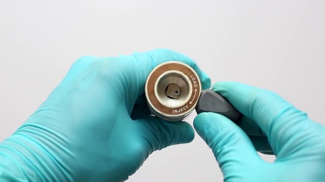 Gloved hands operating a manual HPLC valve, turning the handle to the Inject position for chemical analysis.