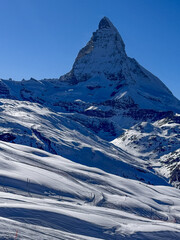 Scenic winter landscape with the matterhorn under a clear blue sky. Bright sun, fresh snow, and alpine terrain create a dramatic view of the Swiss Alps.